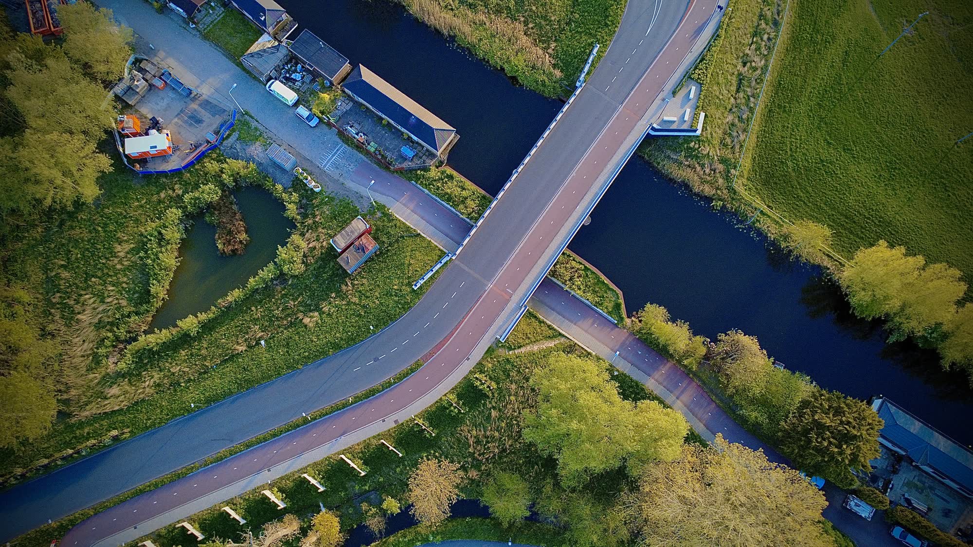 Brug over het water met een fietspad en weilanden, recht van boven