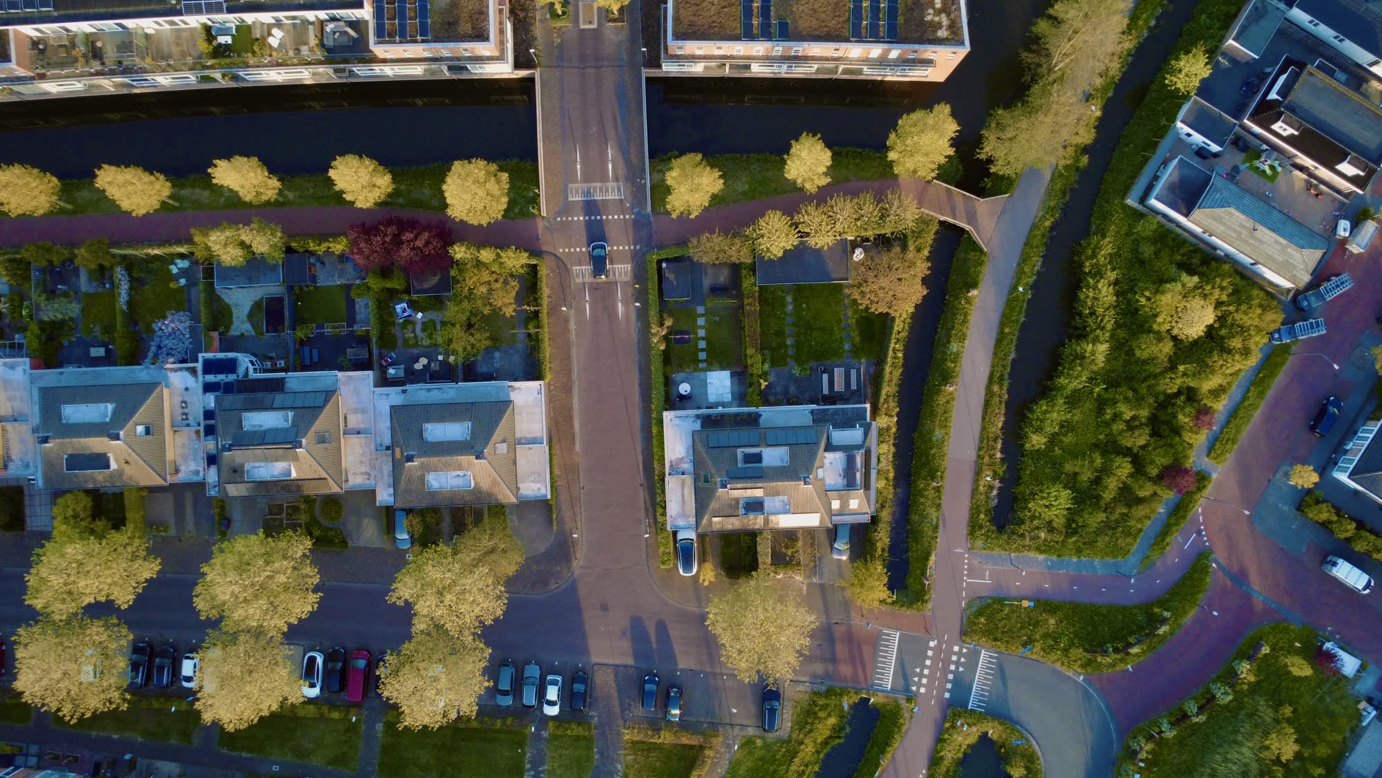 Straat met grachten, bomen en huizen, recht van boven in avondlicht