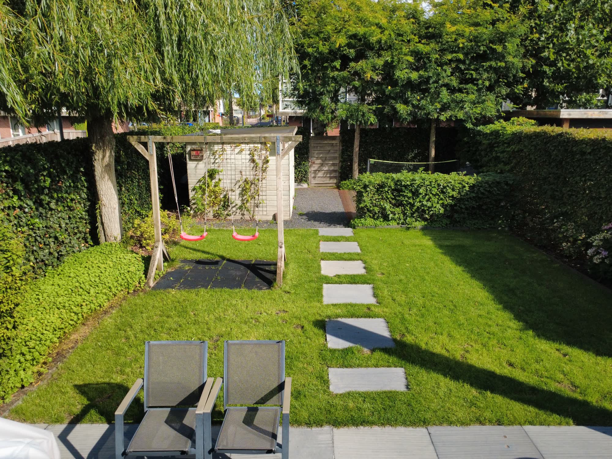 Zicht vanaf het terras door de tuin naar het tuinhuis en de poort