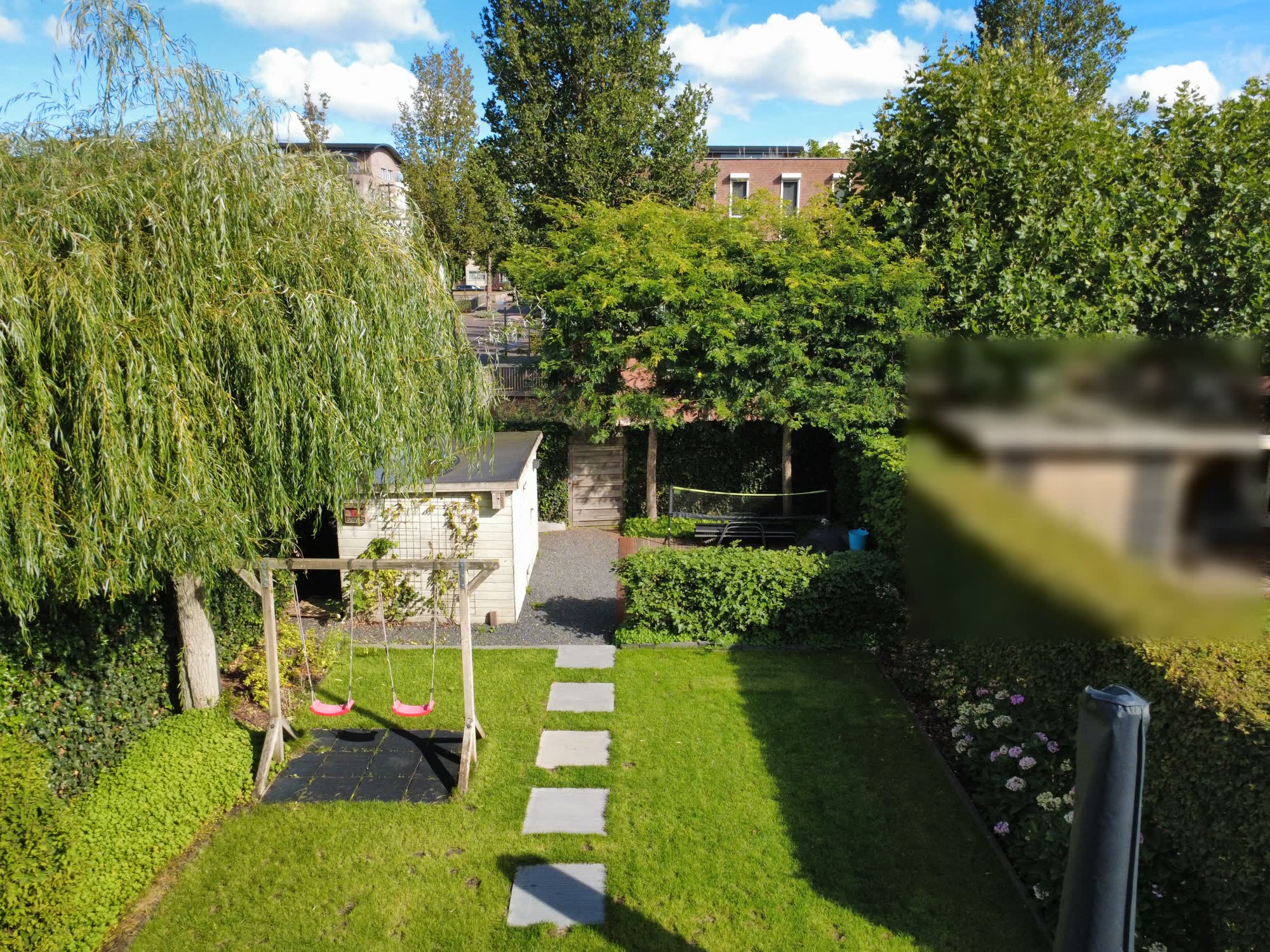 De hele tuin met schommel, tuinhuis en treurwilg