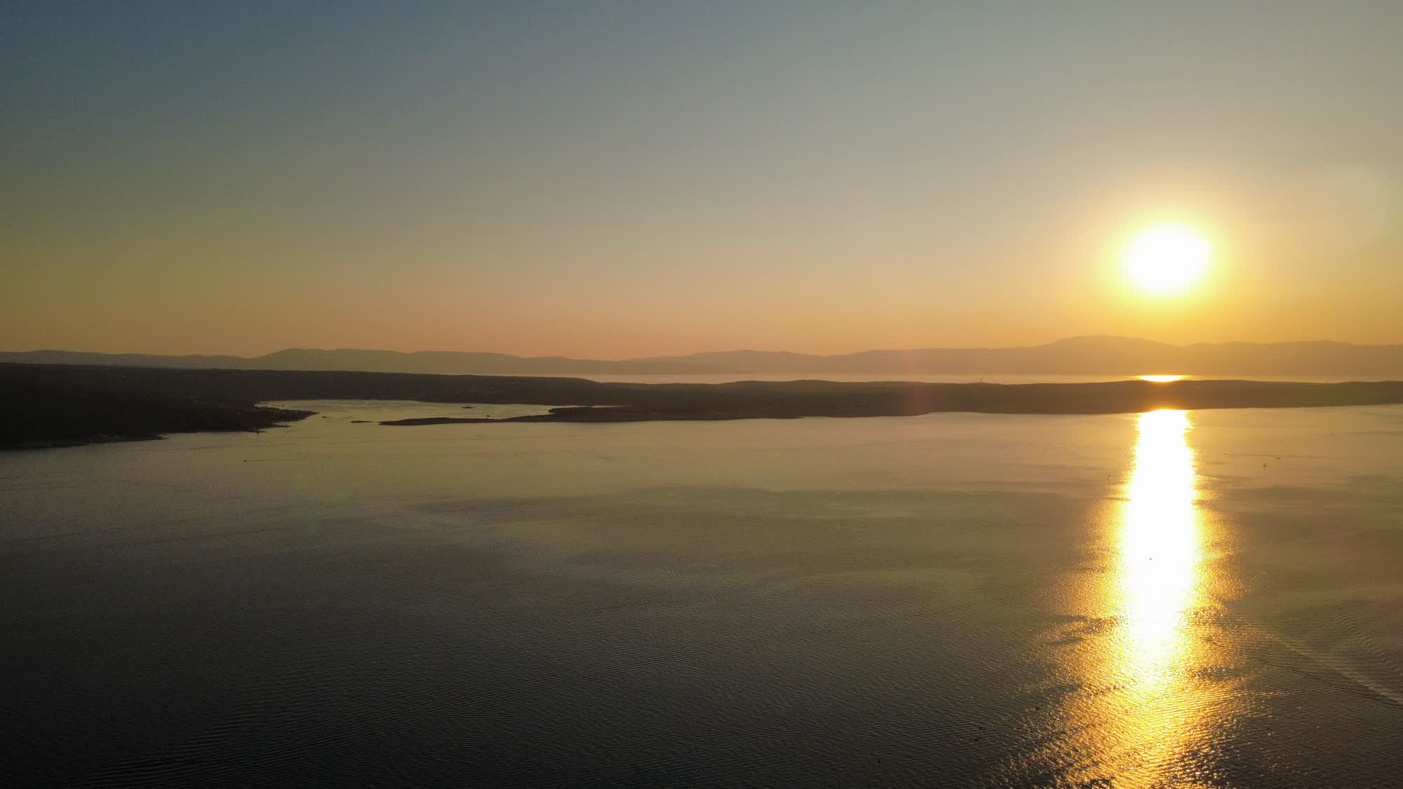 De zon gaat onder boven de zee, met eilanden in de verte
